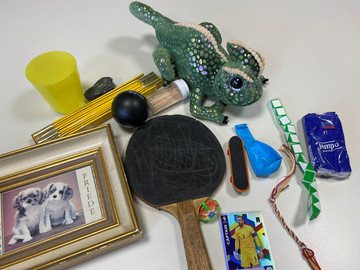 Auf dem Tisch liegen Tischtennischläger, ein Frosch, ein Spielzeugauto, ein Foto von Hundewelpen, Spielzeuge für die Finger