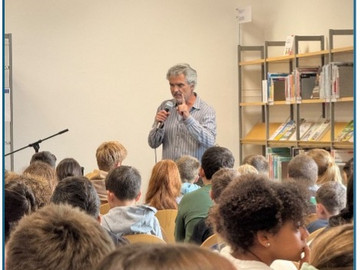 Mann steht am Mikrofon, Schüler sitzen im kreis darum herum